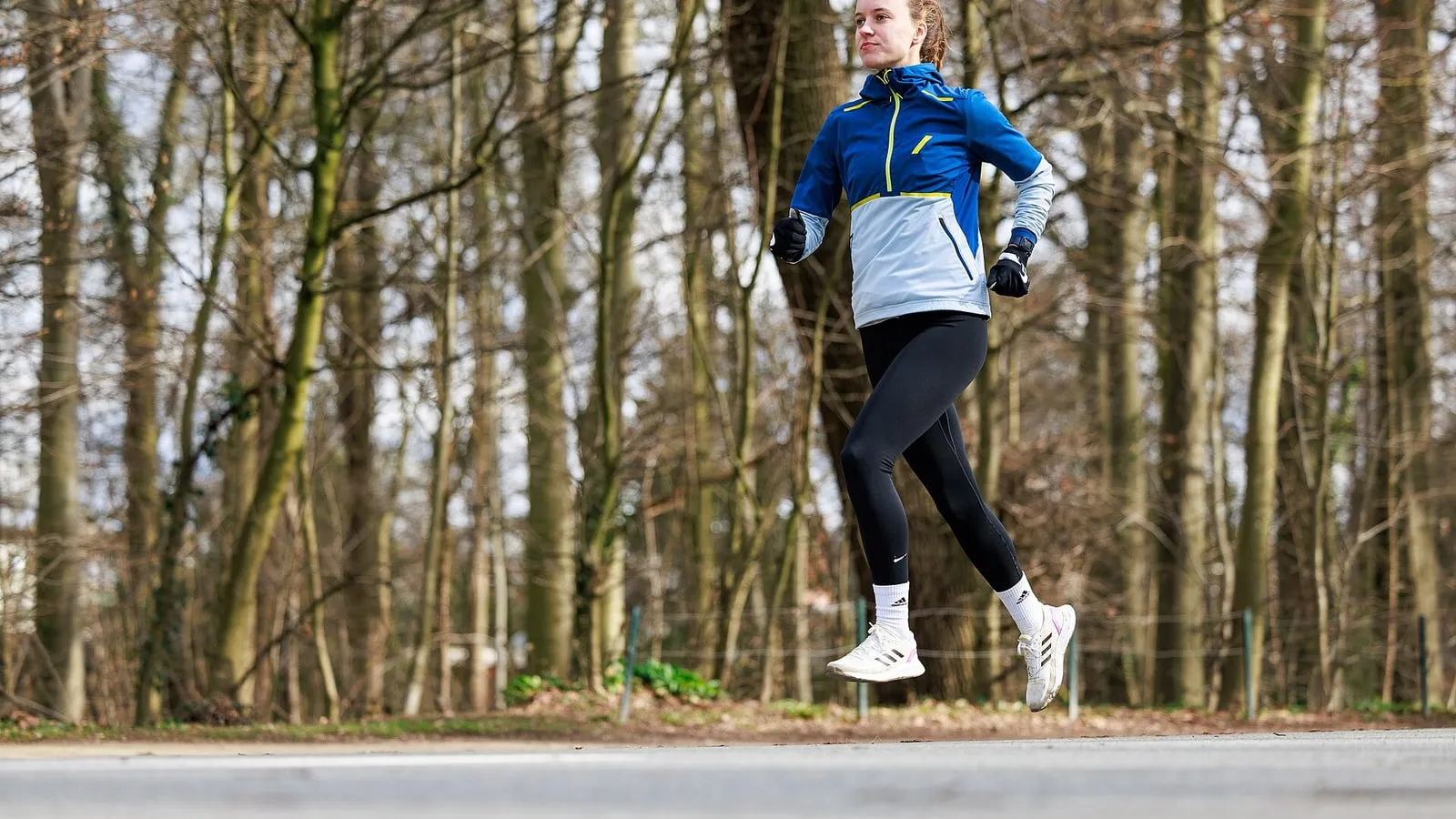 A runner in a light jacket and tights on a park path